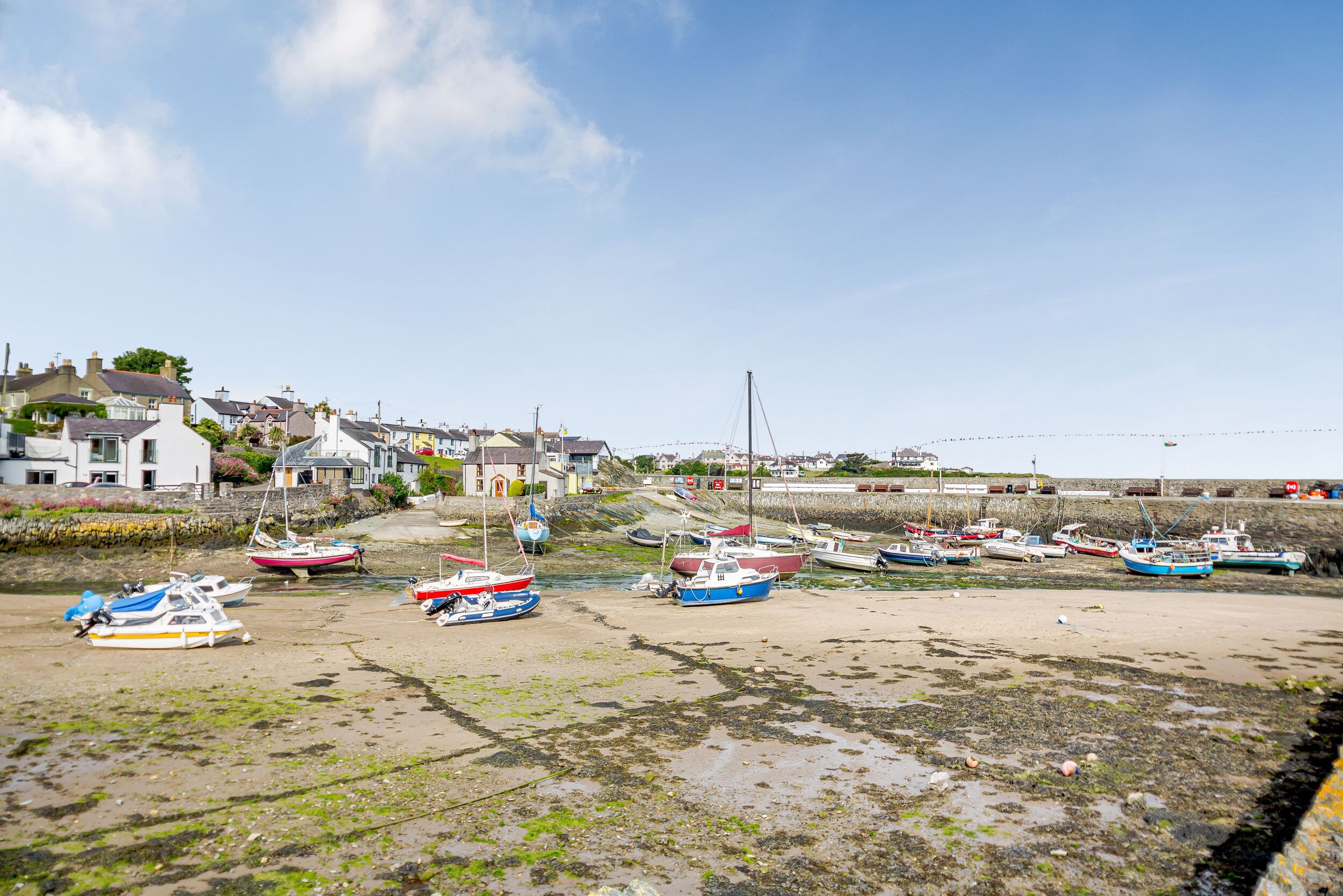 A coastal village with boats docked on a sandy beach, houses in the background, and a clear sky.