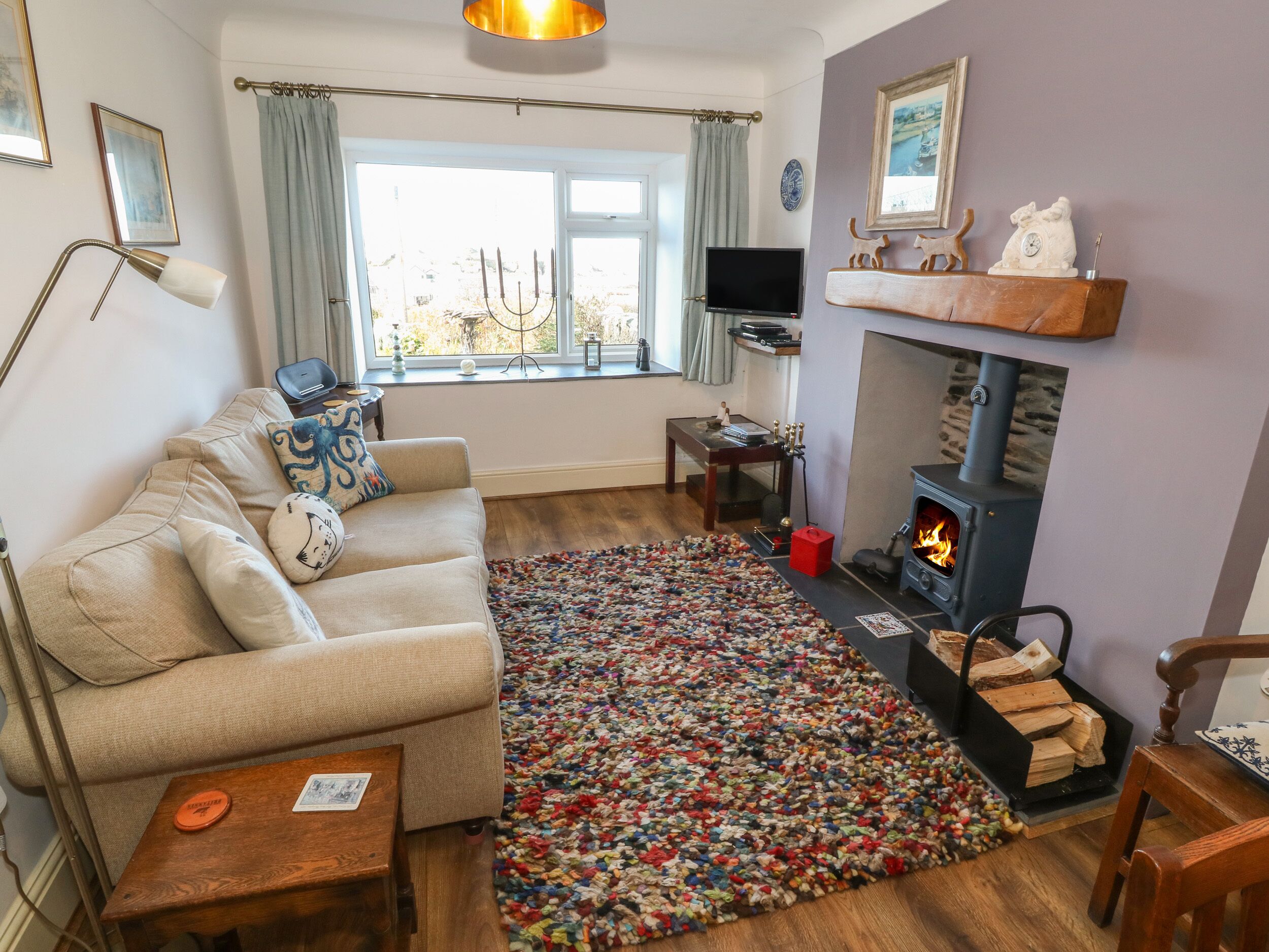A cozy living room with a beige sofa, a colorful rug, a fireplace, and a television.