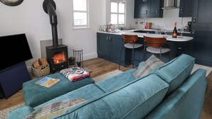 A modern living room with a sofa, a fireplace, and a kitchen area with bar stools. - 126 Main Street (Keighley)