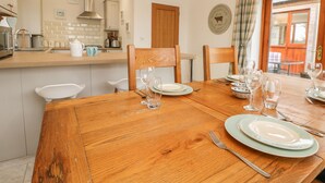 Een eetgedeelte met een houten tafel gedekt voor vier personen, een keuken op de achtergrond en uitzicht op het buitenland door een raam.