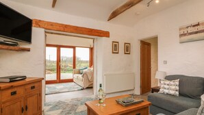 Een woonkamer met een bank, een houten salontafel, een aan de muur bevestigde televisie en een deur naar een balkon.