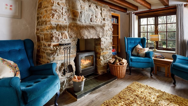 A cozy room with a stone fireplace, wooden beams, and two blue armchairs. - Little Leighs (Launceston)