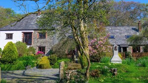 A traditional stone house with a well-maintained garden, including a variety of shrubs and flowering plants. - Little Leighs (Launceston)