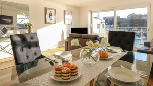 Un espace repas avec une table en verre, des chaises et une vue sur la ville grâce à de grandes fenêtres.
