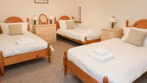 Hotellihuoneessa on kolme puista sänkyä, joissa kaikissa on valkoiset lakanat ja tyynyt, pieni puinen lipasto, yöpöytä lampun kanssa ja seinällä oleva kehystetty kuva.