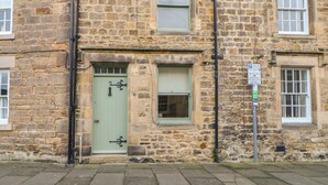 A stone building with a green door and a window. There is a sign on the right side of the building. - Chapel Cottage (Corbridge)