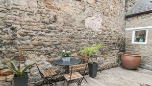 A stone wall, a round table with two chairs, a potted plant, and a large terracotta pot. - Chapel Cottage (Corbridge)