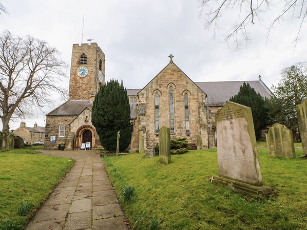 A church with a clock tower, a stone pathway, and a cemetery with headstones. - Chapel Cottage (Corbridge)