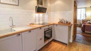 A modern kitchen with white cabinetry, a wooden countertop, a stainless steel range hood, and a built-in oven. - Chapel Cottage (Corbridge)