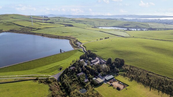 An aerial view of a rural property with a large pond, a wind turbine, and a small cluster of buildings.