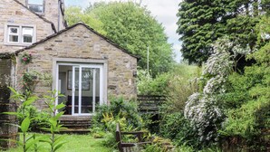 A stone cottage with a wooden bench in a lush garden. - Bridgend Cottage (Skipton)