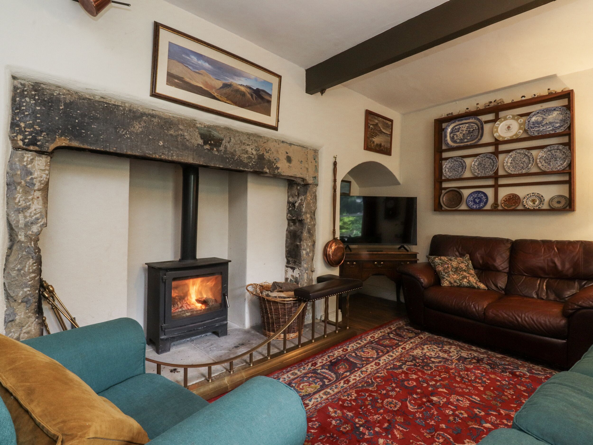 A cozy living room with a fireplace, a television, a brown leather sofa, and a wall-mounted plate rack.