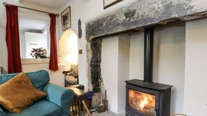 A cozy living room with a blue sofa, a fireplace, and a stone wall. - Bridgend Cottage (Skipton)