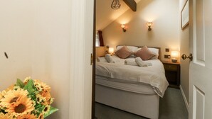A bedroom with a bed, bedside tables, a nightstand, a lamp, and a window. - Bridgend Cottage (Skipton)