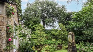 A stone pathway leading through a lush garden with various plants and a rustic stone structure. - Bridgend Cottage (Skipton)