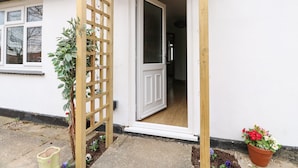 A white house with a wooden door and a wooden trellis with plants.