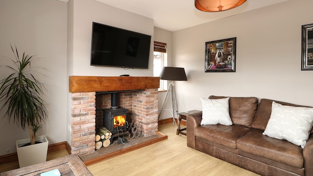 A living room with a brick fireplace, a brown leather sofa, a television mounted on the wall, and a floor lamp.