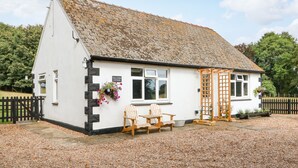 A white cottage with a stone roof, a wooden door, and a sign reading "Hall Farm Cottage".