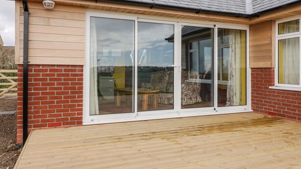 A house with a large sliding glass door, a brick exterior, and a wooden deck. - Orchard Chalet (Liskeard)