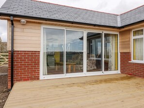 A house with a large sliding glass door, a brick exterior, and a wooden deck. - Orchard Chalet (Liskeard)