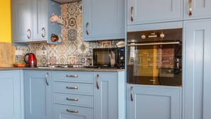 A kitchen with light blue cabinets, a microwave, a stove, and a red kettle. - Orchard Chalet (Liskeard)