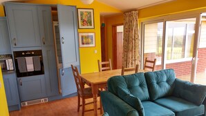 A compact living space with a dining area, kitchenette, and a sofa. - Orchard Chalet (Liskeard)