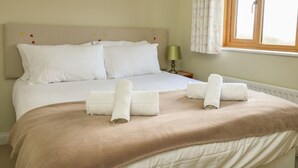 Un lit bien fait, avec du linge de lit blanc et une couverture beige, une lampe de chevet et une fenêtre avec des rideaux.