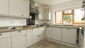 Une cuisine moderne avec des meubles blancs, une hotte de cuisinière en acier inoxydable, une fenêtre donnant sur un espace verdoyant et un plan de travail sur lequel se trouvent un grille-pain et une casserole.