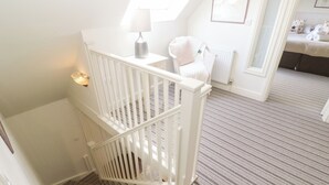En trappe med hvid gelænder fører op til et soveværelse med et stribet tæppe, en hvid radiator og et natbord med en lampe.
