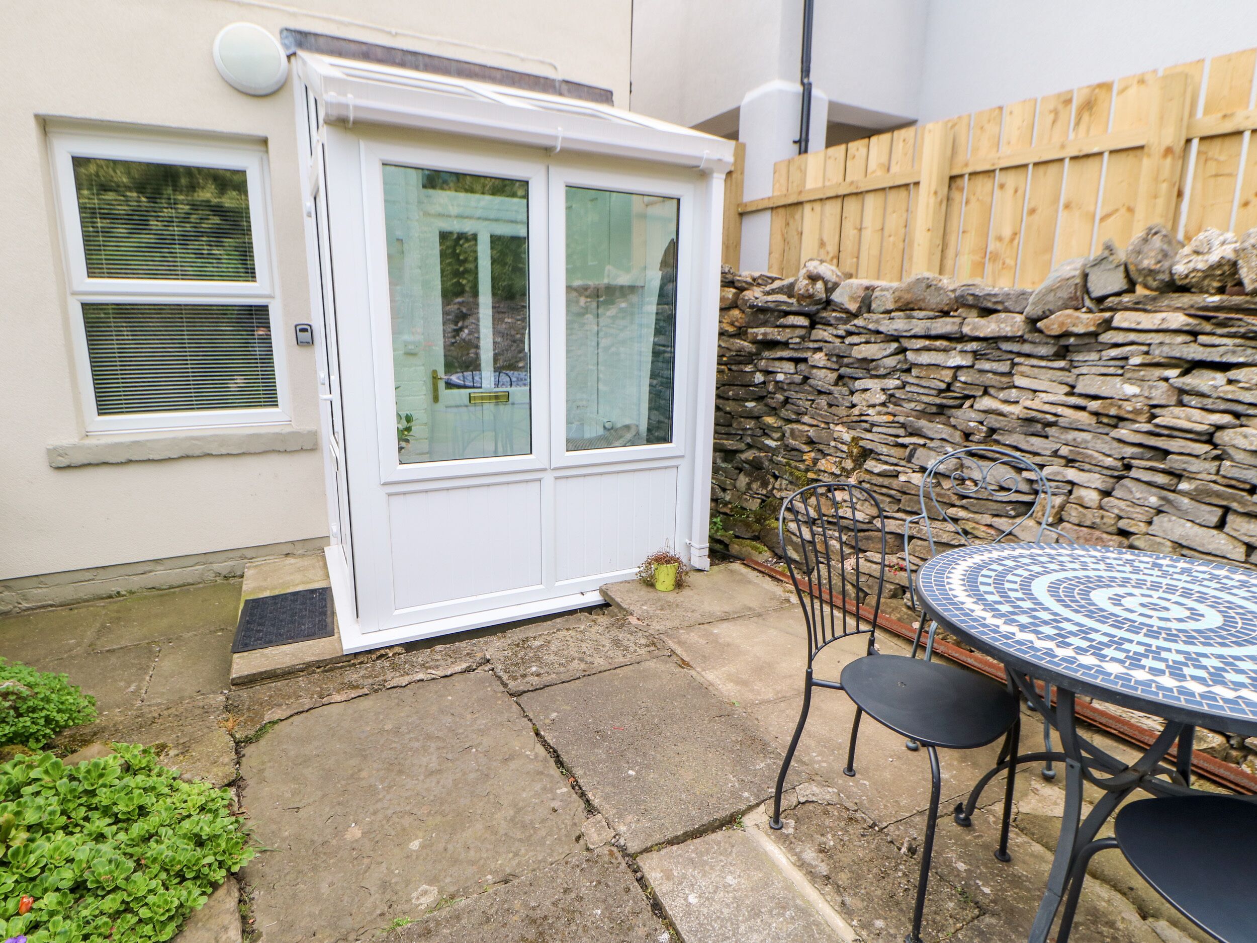 A patio with a stone wall, a white door, and a round table with chairs.