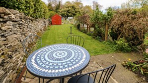 A round table with a mosaic tile design, a stone wall, and a red shed in a garden. - Daisy Cottage (Leyburn)