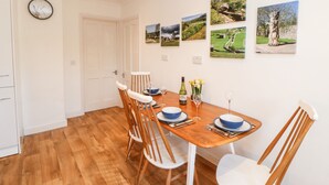 A dining area with a wooden table, white chairs, and a white door. - Daisy Cottage (Leyburn)