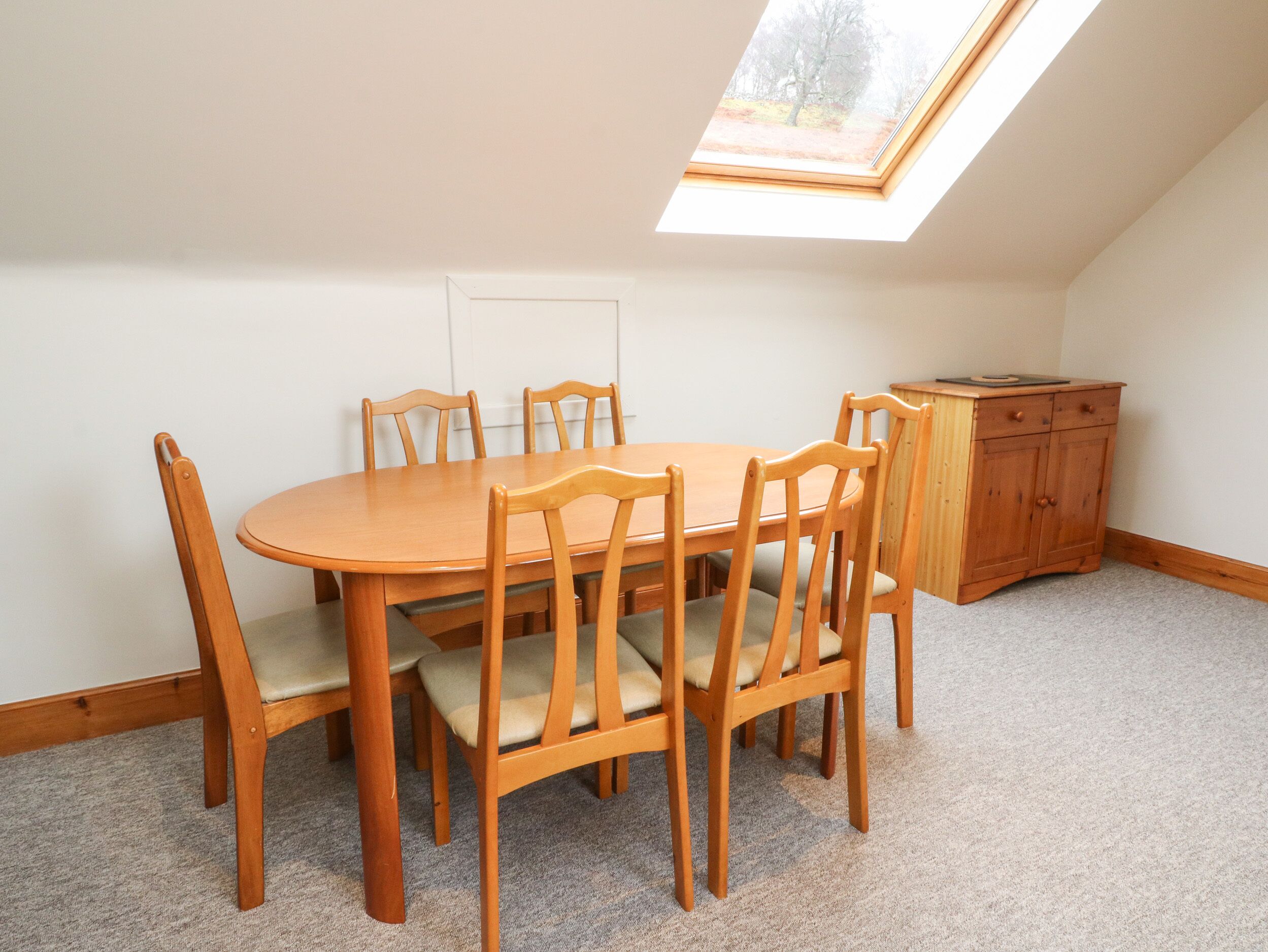 A dining area with a wooden table and chairs, a small cabinet, and a skylight.