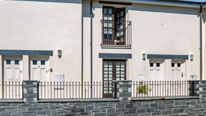 Un immeuble de deux étages avec des portes numérotées, un balcon et un mur de pierre à l’avant.