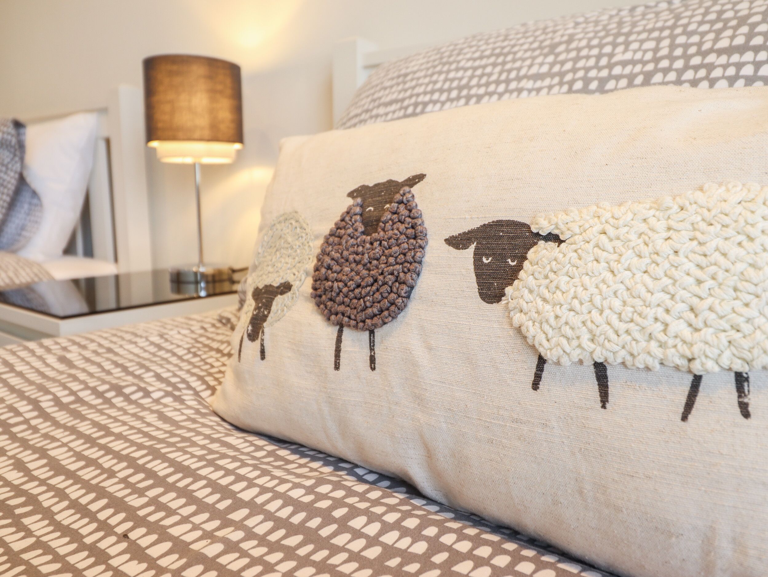 Un letto con una coperta a fantasia e un cuscino con un disegno di una pecora lavorata a maglia.