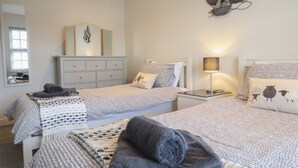 Une chambre avec deux lits, une commode, un miroir et une œuvre d’art accrochée au mur.