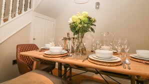 Een eethoek met een houten tafel gedekt voor zes personen, omringd door comfortabele stoelen. Op de tafel staat een vaas met bloemen, en erboven hangt een kroonluchter.