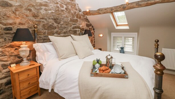 Een slaapkamer met een stenen muur, een houten bed, een nachtkastje, een dienblad met ontbijtartikelen en een dakraam.