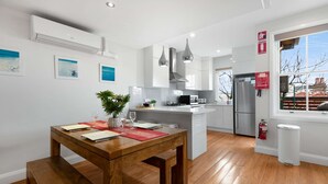 Une cuisine moderne dotée d’un îlot central, d’appareils électroménagers en acier inoxydable, de luminaires suspendus et offrant une vue sur l’extérieur.