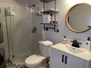 A bathroom with a glass-enclosed shower, a toilet, a sink with a mirror, and shelves with toiletries. - Moyie Lake Cabin (Moyie)