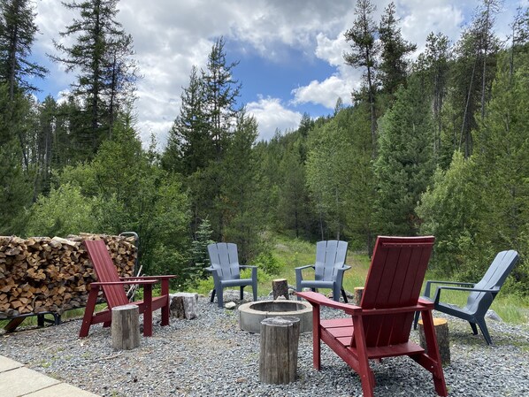 A forested outdoor seating area with Adirondack chairs and a fire pit. - Moyie Lake Cabin (Moyie)