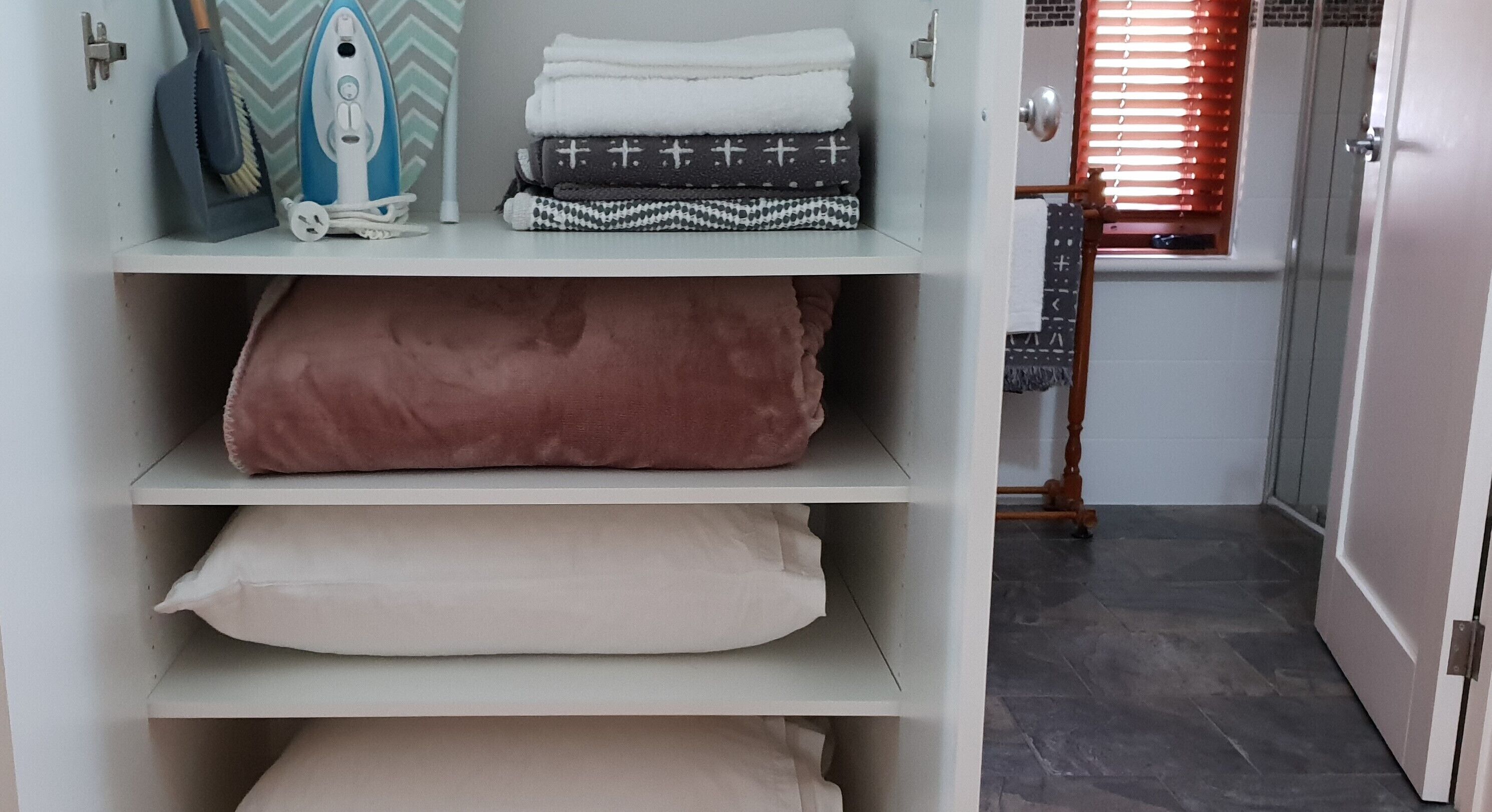 Un espace de rangement avec des étagères où sont pliées des serviettes, ainsi qu’un sèche-cheveux et une brosse.