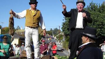 Une scène de rue avec deux hommes vêtus de costumes d’époque, l’un tenant un fouet et l’autre un chien.