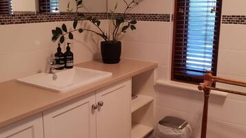A bathroom with a white sink, a potted plant, a hand soap dispenser, and a window with blinds.