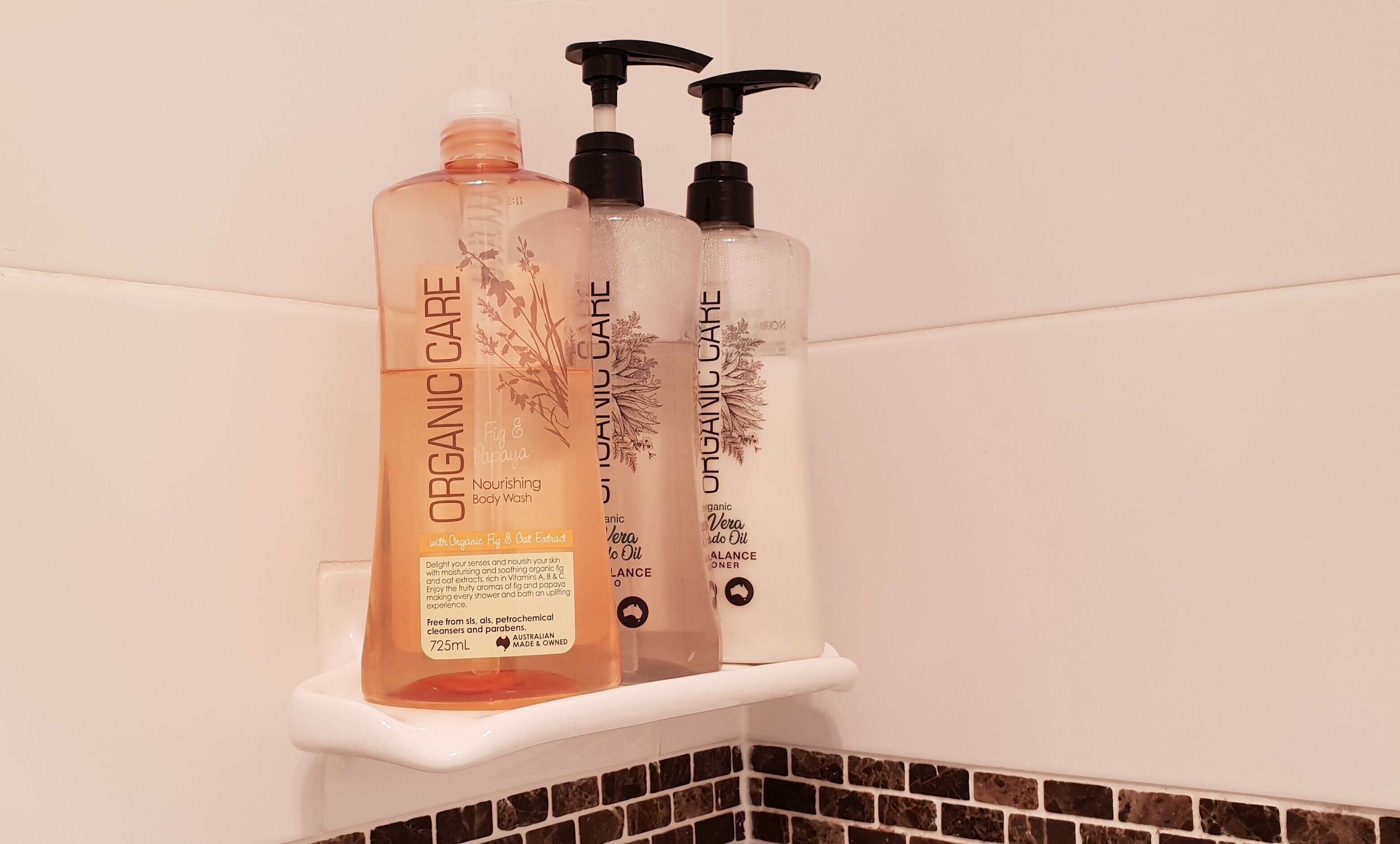 Tres botellas de exfoliante corporal Orgánico Care sobre un estante blanco.