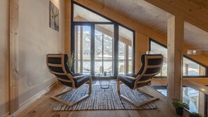 Ein Zimmer mit hohen Decken, Holzbalken, großen Fenstern und zwei schwarz-weiß gestreiften Stühlen.