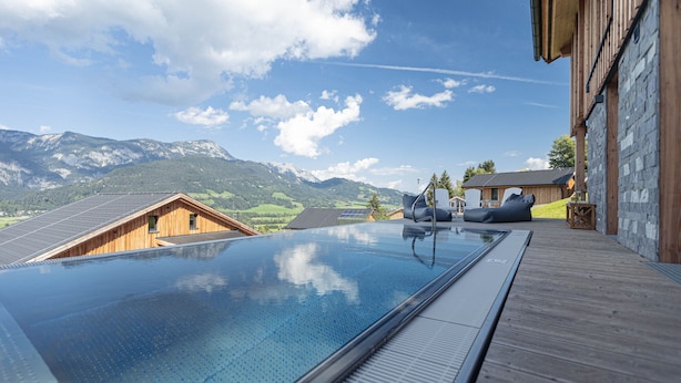 A swimming pool with a wooden deck, a stone building, and mountains in the background. - Superior Chalet with 5 bedrooms, sauna & pool (Haus im Ennstal)