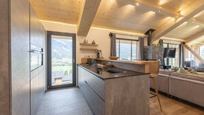 A modern kitchen with a large island, wooden beams, and a view of the mountains. - Superior Chalet with 5 bedrooms, sauna & pool (Haus im Ennstal)