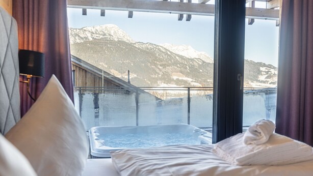 Habitación de hotel con cama, jacuzzi y vista a la montaña.