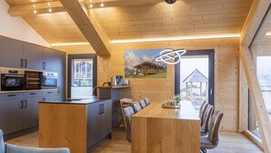 Una cocina moderna con electrodomésticos integrados, un comedor con mesa y sillas de madera, y un ventanal con vistas a la montaña.